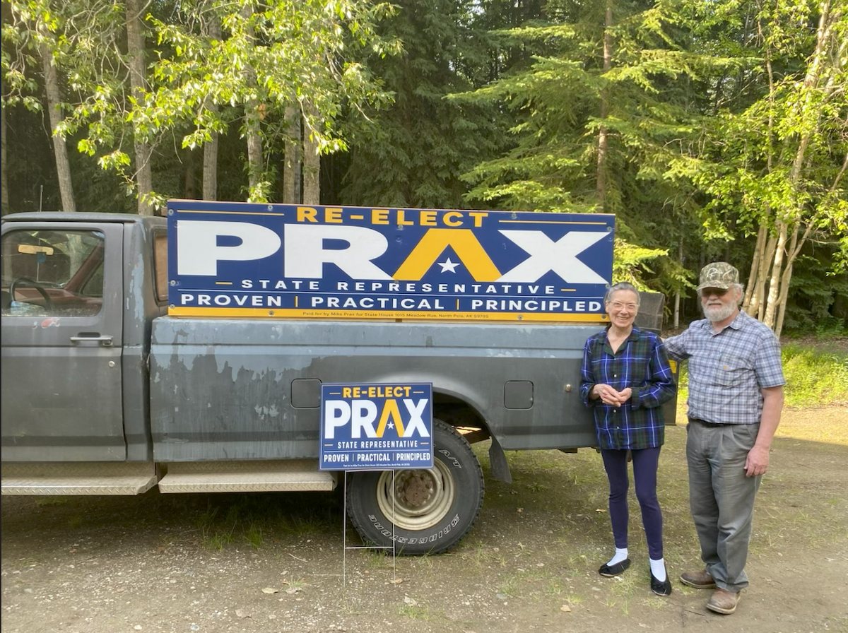 Mike Prax and his wife Elaine beside a truck carrying a large Re-Elect Prax campaign banner.